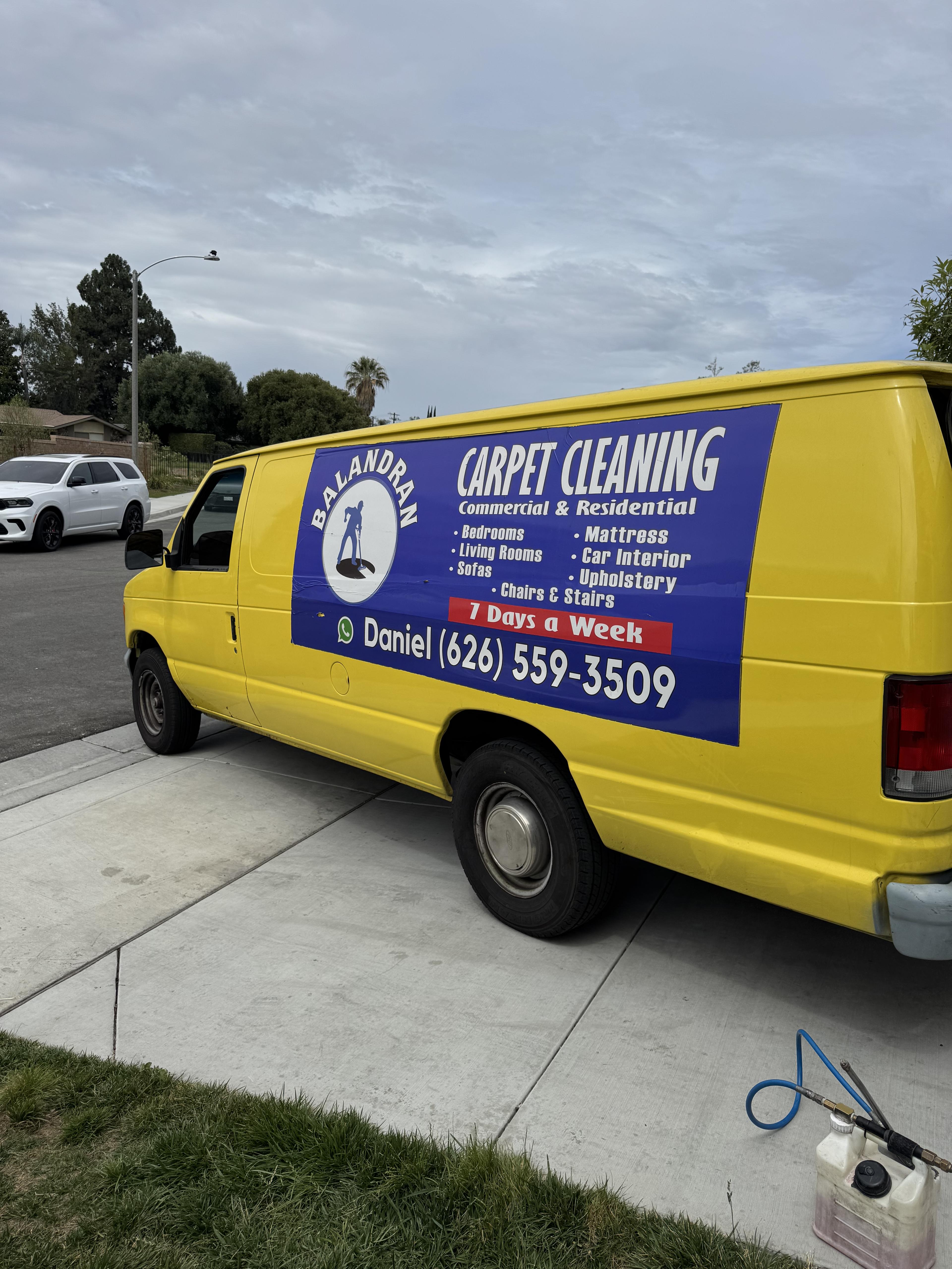 Camioneta amarilla con logotipo de Balandran Carpet Cleaning estacionada en la calle.